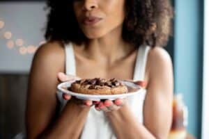 A woman holding a plate with a large chocolate cookie. Learn how to manage cravings like this!