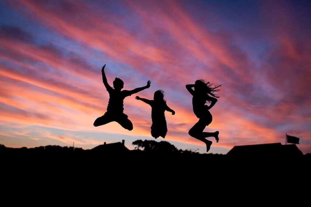 Three people jump for joy against the sunset after achieving health goals.