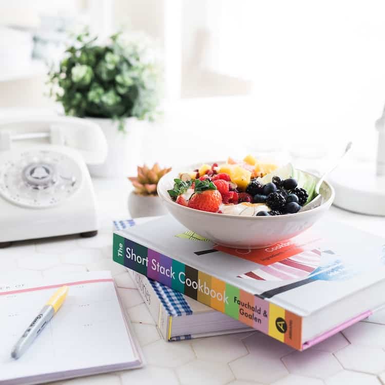 Bowl of fruits on a stack of books next to an open notebook