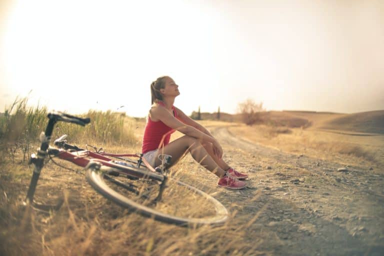 Woman sitting in a field in the sunshine next to her bicycle.
