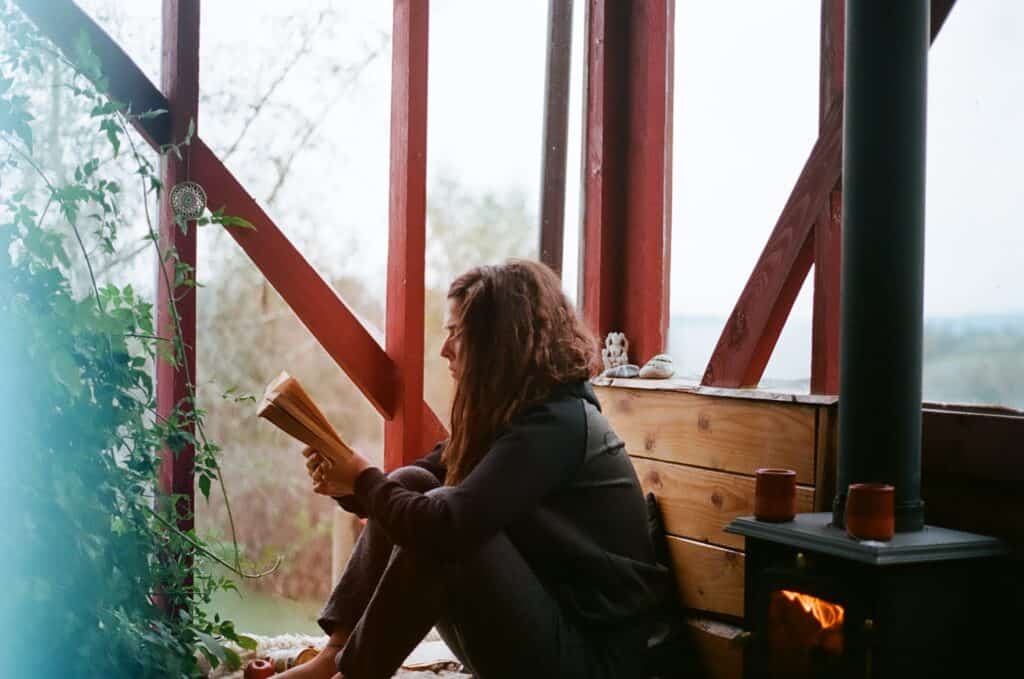 A woman sits by a window and reads a book. She is trying to be more mindful