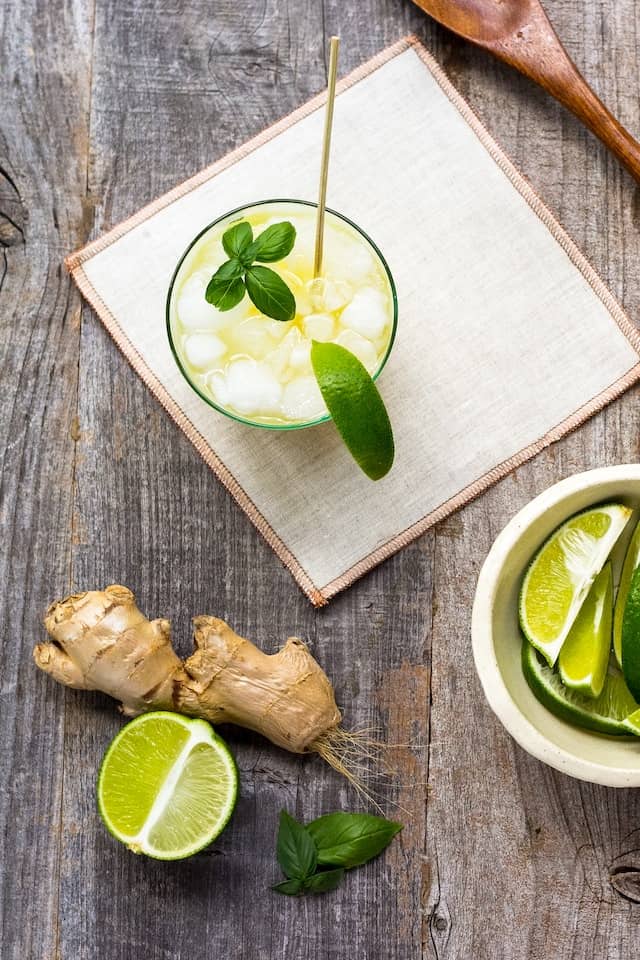 A refreshing summer ginger drink in a glass surrounded by ginger and limes