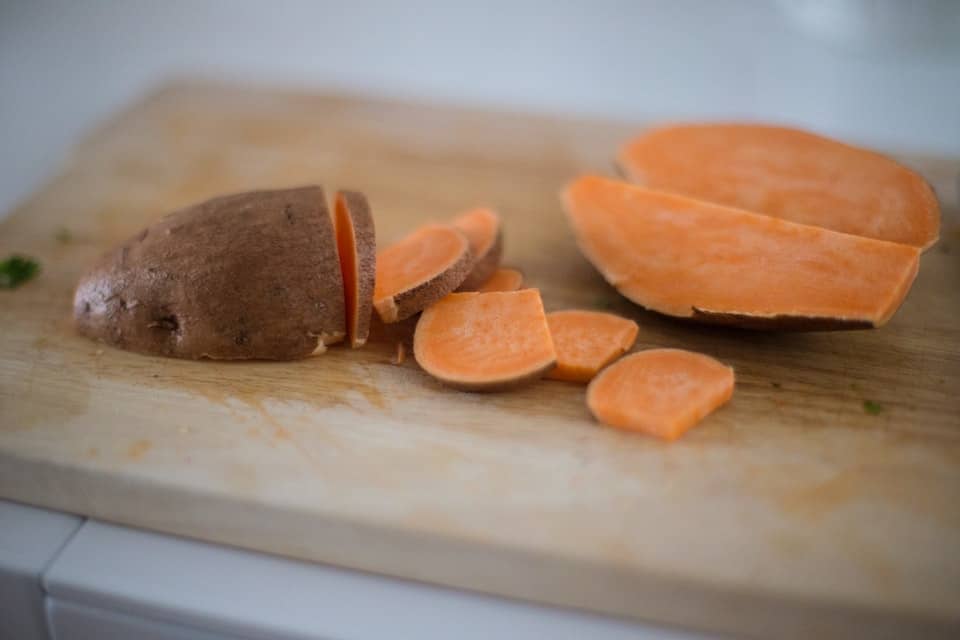 Sweet potatoes being chopped on a wooden board.